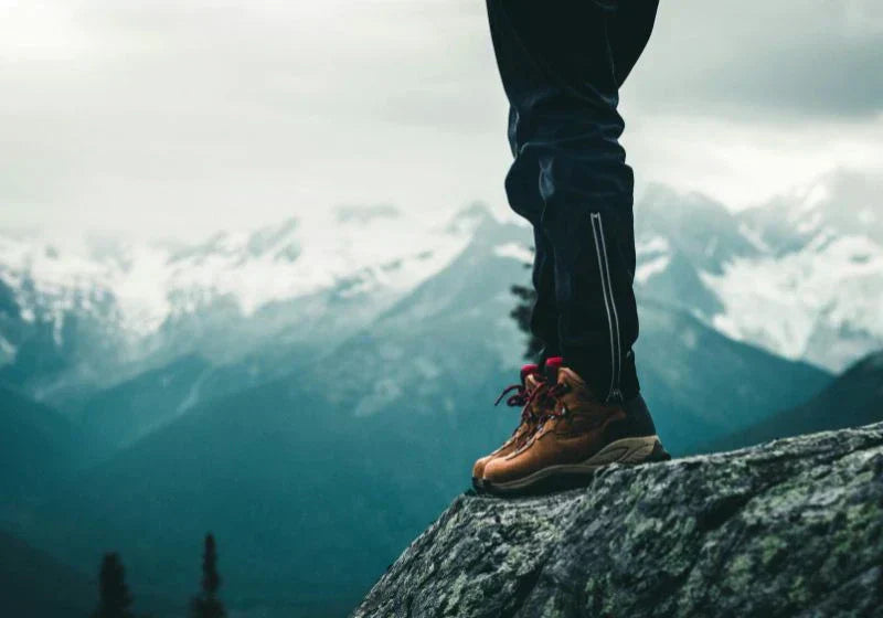Hiker wearing trekking shoes standing on rocky cliff with mountain view.
