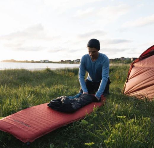 Man setting up camping gear on grassy field near lake at sunset